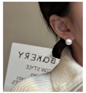 Close-up of matte white spherical stud earring on model with a beige knit sweater