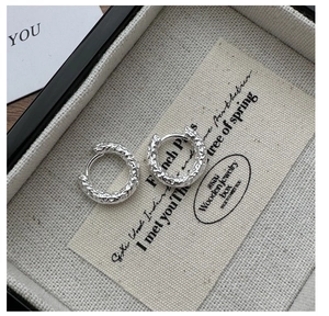 Detailed macro view of silver hoop earrings with a unique hammered texture on linen