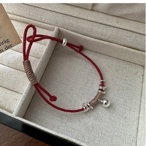 Dettaglio del bracciale cordino rosso intrecciato con perline argentate e campanellino