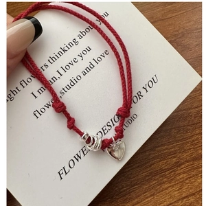 Detail of red braided string bracelet with silver heart charm and adjustable sliding knot