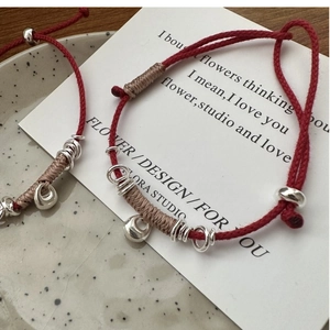 Detail of red string bracelet with silver beads on a card and ceramic plate