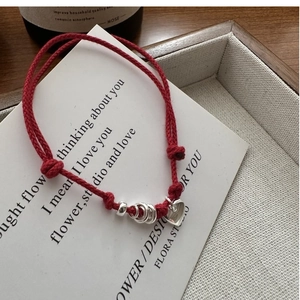 Macro shot of minimalist red rope bracelet featuring silver heart charm on card