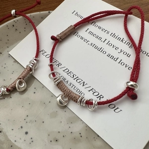 Handcrafted woven red string bracelets with S925 silver pendants on a ceramic tray