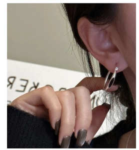 Nahaufnahme eines minimalistischen Silberohrrings mit poliertem Finish am Ohr eines Modells