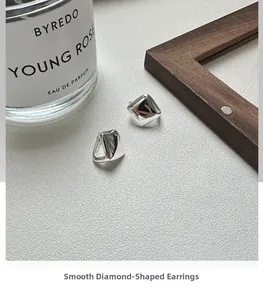Detail shot of minimalist silver rhombus hoop earrings on a textured lifestyle surface