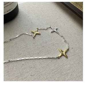 Détail macro d'une chaîne en argent 925 avec pendentifs étoiles dorés sur tissu en lin