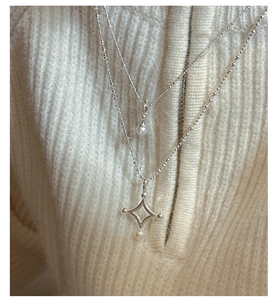 Détail de colliers en argent S925 à perles et pendentifs étoile sur un pull en maille
