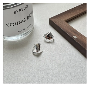 Macro shot of polished silver geometric square hoop earrings on a minimalist white surface
