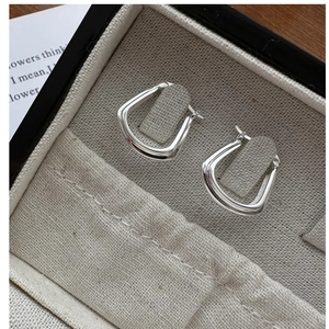 Vue macro des boucles d'oreilles carrées en argent S925 sur boîte à bijoux en velours beige