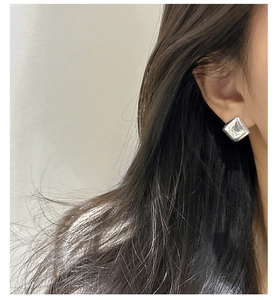 Detail of square silver earring with irregular fluid metal texture on female ear