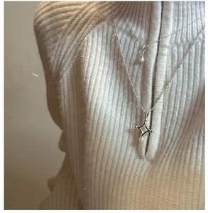 Détail d'un collier double rang argenté avec perles et pendentif étoile sur pull blanc