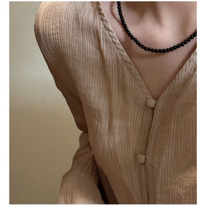 Close-up of a glossy black agate beaded necklace on a model with a beige V-neck cardigan
