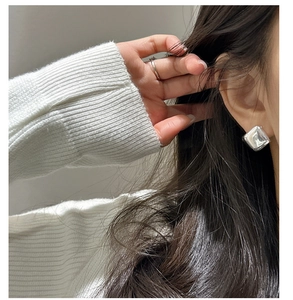 Close-up of a minimalist silver square hoop earring worn on an ear with polished finish