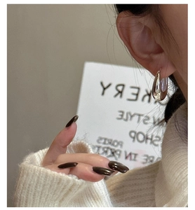 Close-up of polished silver U-shaped hoop earrings on model wearing a beige sweater