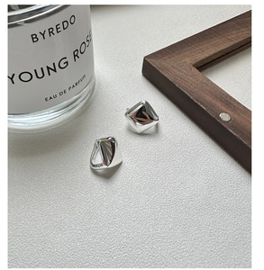 Macro detail of geometric square silver earrings on a minimalist textured surface