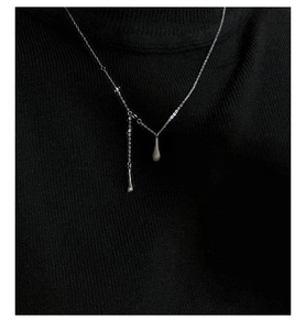 Détail du collier à double pendentif goutte d'argent sur un pull en tricot noir