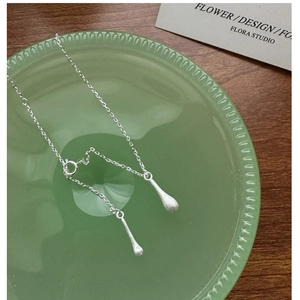 Détail de doubles pendentifs goutte d'eau au fini argent brossé sur une chaîne fine