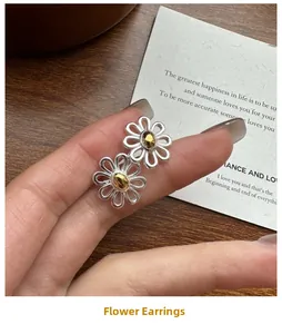Close-up of S925 sterling silver daisy stud earrings held by hand for scale