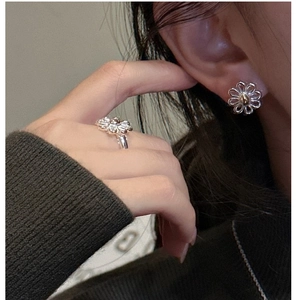 Detailed view of silver daisy stud earrings and ring with gold accents worn by a model