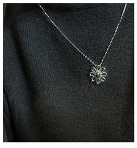 Detail of S925 silver daisy necklace pendant worn on a dark grey knit sweater