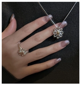Detail view of S925 silver daisy ring and necklace set on a textured grey sweater