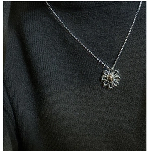 Detailed view of an S925 silver daisy pendant necklace worn over a grey knit sweater