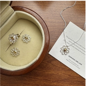 Detail of S925 silver daisy jewelry set with necklace and ring on a wooden background