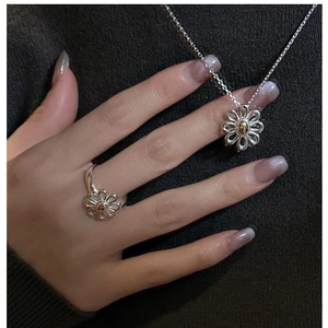 Close-up of S925 silver daisy pendant and matching ring on a green knit background