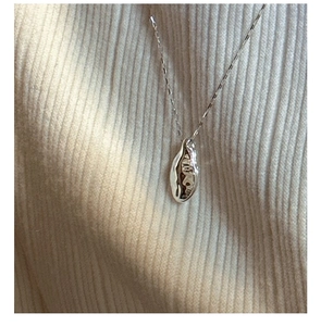 Macro detail of irregular lava-textured silver pendant on a fine necklace over a knit sweater