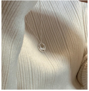 Detail of 925 sterling silver donut pendant on a slim chain worn on a cream knit sweater