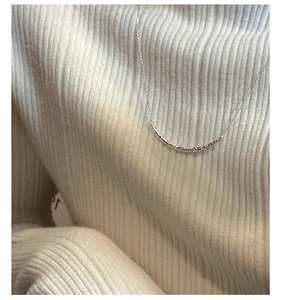 Gros plan d'un collier pendentif sourire argenté avec texture martelée sur pull en maille blanc