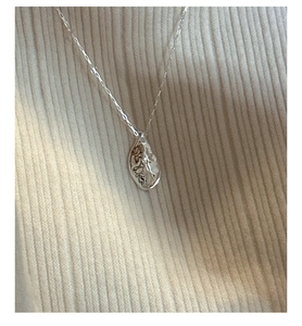 Macro shot of silver water drop pendant with textured finish on white knit fabric