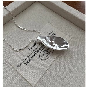 Macro detail of silver necklace with textured liquid metal pendant on linen display