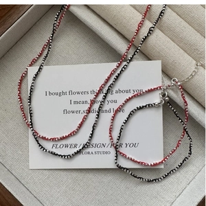 Détail du collier chaîne en corde tressée rouge et noir avec perles argentées sur carte