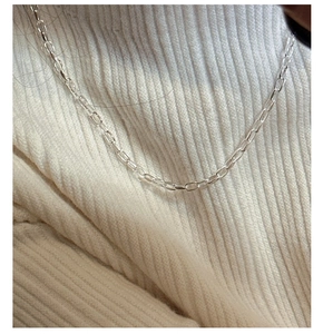 Collier trombone en argent porté sur un pull en maille beige pour un style minimaliste
