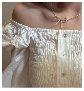 Close-up of S925 silver bow necklace on model wearing a white off-shoulder ruffled top