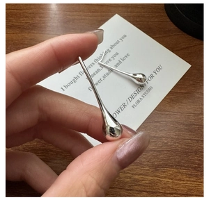 Detail of hand holding a minimalist S925 sterling silver teardrop earring on a wood desk