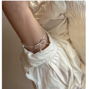 Close-up of a delicate S925 silver bow bracelet worn on a wrist with an elegant cream sleeve