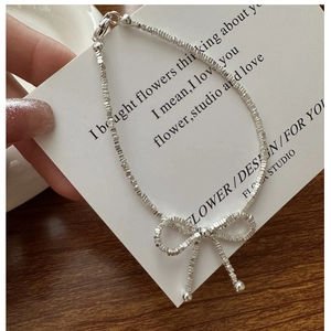 Macro view of silver bow pendant and faceted metallic beads on minimalist necklace