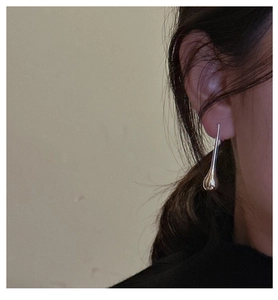Close-up of minimalist silver teardrop earring with polished finish on ear