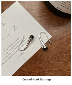 Minimalist silver curved hook earrings with black beads on a wooden artistic background