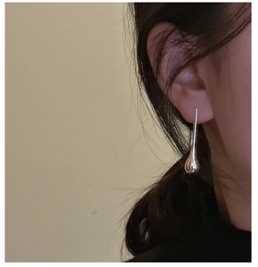 Close-up of minimalist S925 silver water drop earrings on model in warm lighting