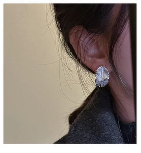 Detailed close-up of a silver feather-shaped stud earring worn on the earlobe