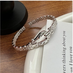 Detailed close-up of a silver buckle bangle with horseshoe texture on a white plate