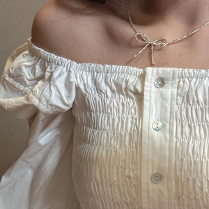 Elegant S925 silver bow necklace on a woman wearing a white smocked off-shoulder top