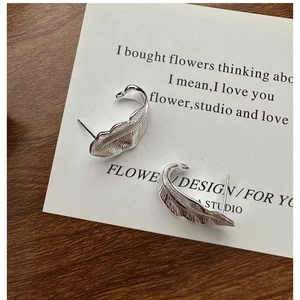 Detailed view of silver feather stud earrings with elegant swan neck curve and texture