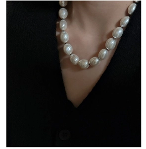 Primo piano di una collana con grandi perle barocche bianche indossata su un maglione nero