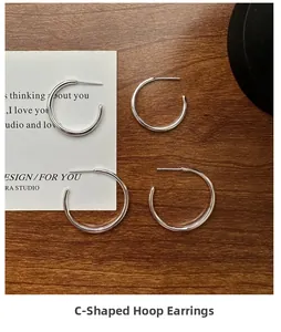 Detailed view of silver S925 minimalist C-shaped hoop earrings on dark wooden background