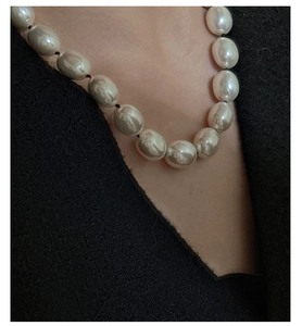 Dettaglio di una collana con grandi perle barocche e filo nero annodato a mano su abito