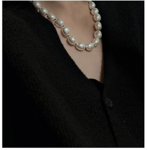 Dettaglio di una collana con grandi perle ovali su un cardigan nero strutturato